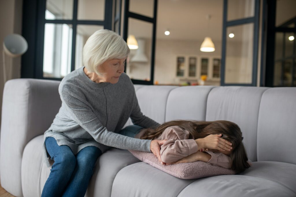 Angry little girl lying on the couch and sitting grandmother.