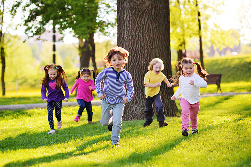 many young children smiling running along the grass in the park. Childhood, Children's Day, vacation, vacation, adventure, friendship.